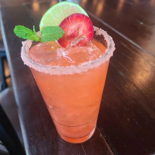 Strawberry margarita with lime, mint, and a sugared rim on a dark wooden table.