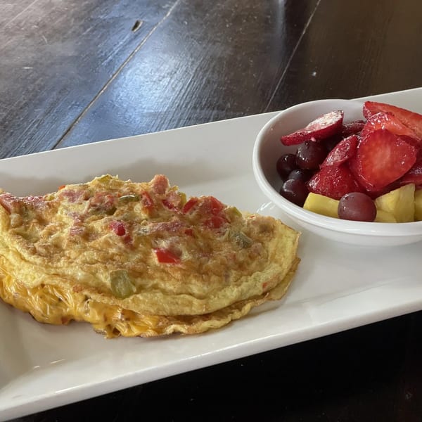 A cheese omelet with bell peppers and a side of fresh fruit on a white rectangular plate.