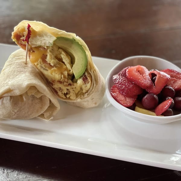 Breakfast burrito with scrambled eggs, cheese, and avocado, served with a side of fresh fruit.